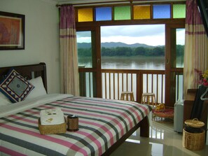 A bedroom with a bed, a view of a lake, and a balcony with wicker furniture.