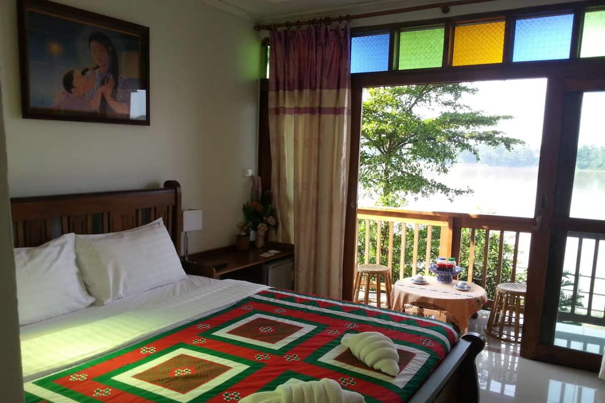 Ein Hotelzimmer mit Bett, Nachttisch, Fenster mit Seeblick und Balkon mit Tisch und Stühlen.