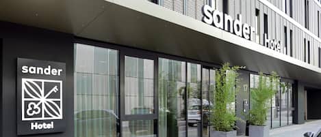 A hotel exterior with a modern facade, large windows, and a sign indicating it's the 'sander Hotel'.