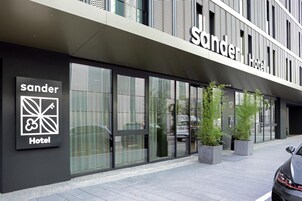 Exterior de un hotel con fachada moderna, ventanas grandes y un cartel que indica que es el Hotel Sander.
