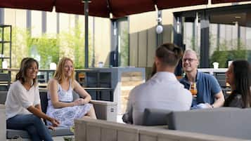 Eine Gruppe von Menschen sitzt in einem Straßencafé unter einem roten Sonnenschirm.