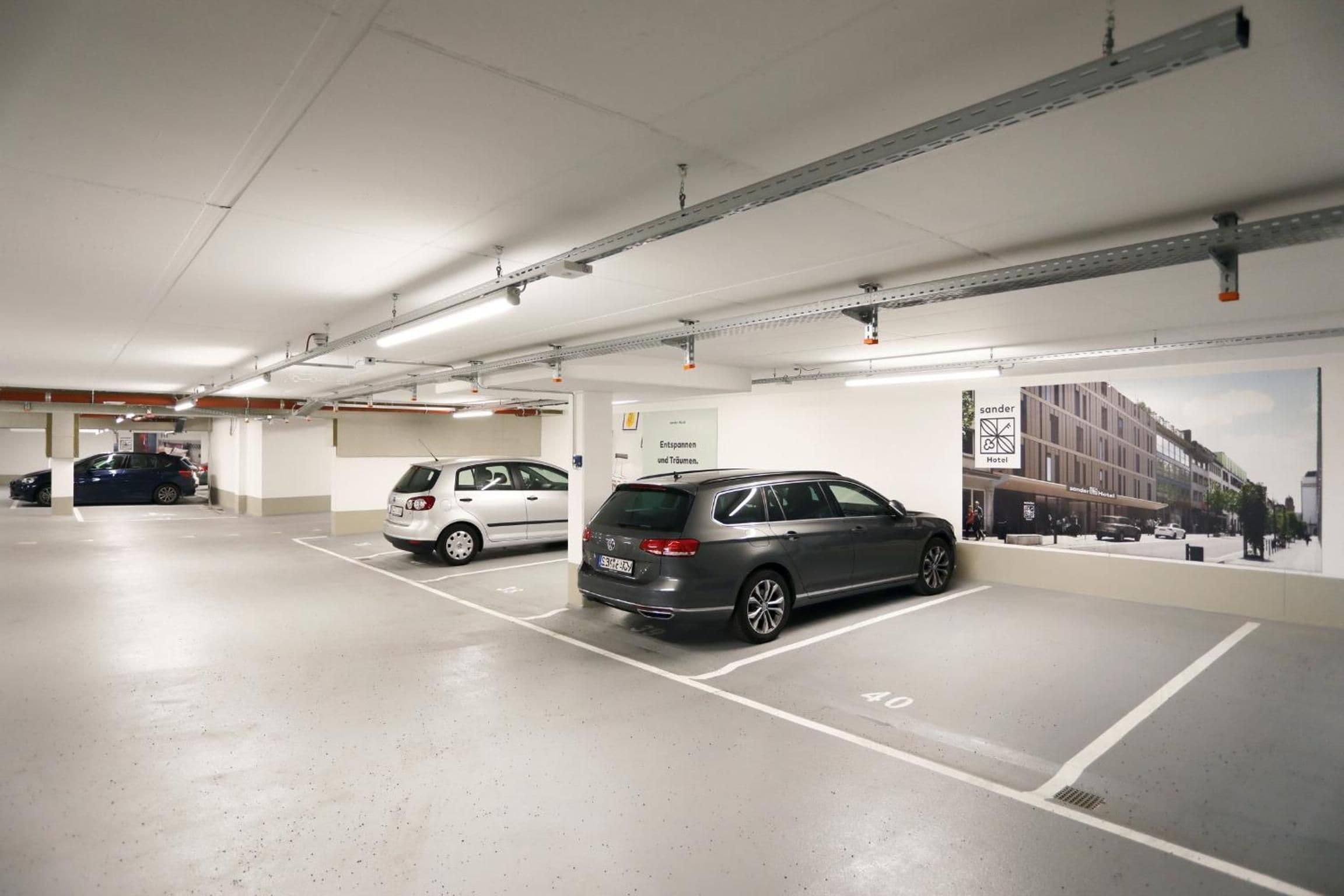 A parking garage with multiple parking spaces, a white van, and a grey car parked.