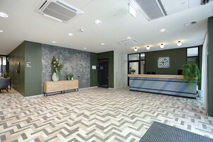 Zona de recepción de hotel con un diseño moderno, que incluye un mostrador, un banco y un suelo estampado.