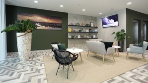Un hall d’entrée moderne agrémenté d’un grand tableau, d’un comptoir d’accueil, de sièges confortables et d’un écran de télévision.