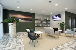 Un vestíbulo moderno con un cuadro grande, un mostrador de recepción, asientos cómodos y una pantalla de televisión.