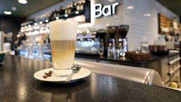 A bar setting with a glass of a light-colored beverage on a coaster, a spoon, and coffee beans on a small plate.