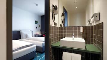 Habitación de hotel con dos camas, baño con lavamanos y espejo.