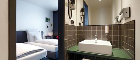 A hotel room with two beds, a bathroom with a sink, and a mirror.