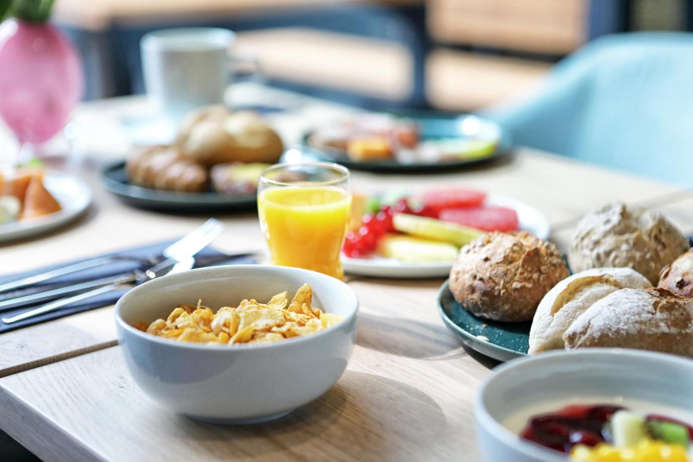 A breakfast setting with cereal, pastries, and a glass of orange juice on a wooden table.