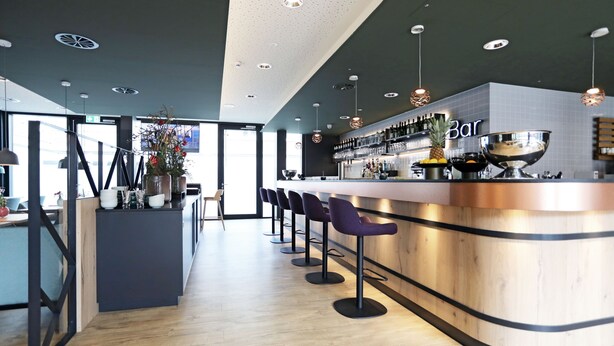 Un espace bar moderne doté d’un comptoir incurvé, de tabourets de bar et d’une variété de bouteilles et de verres.