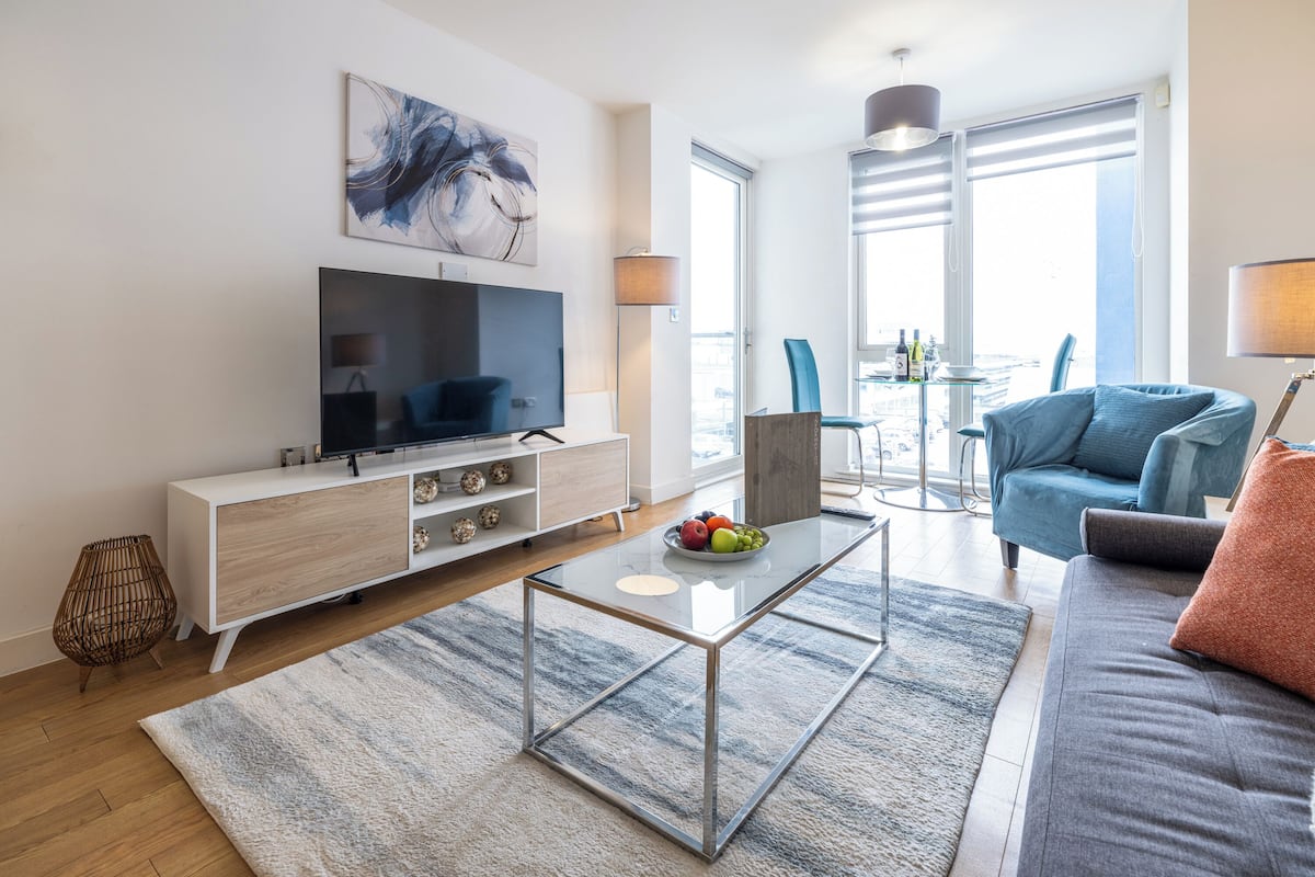 Una sala de estar moderna con una televisión de pantalla plana, una mesa de centro de vidrio, un sofá y un comedor con mesa y sillas.