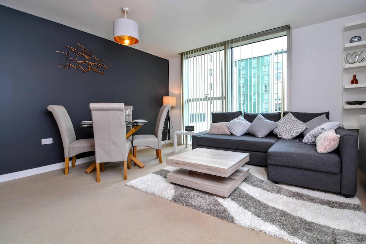 Una sala moderna con un sofá gris, dos sillones, una mesa de centro y una alfombra.