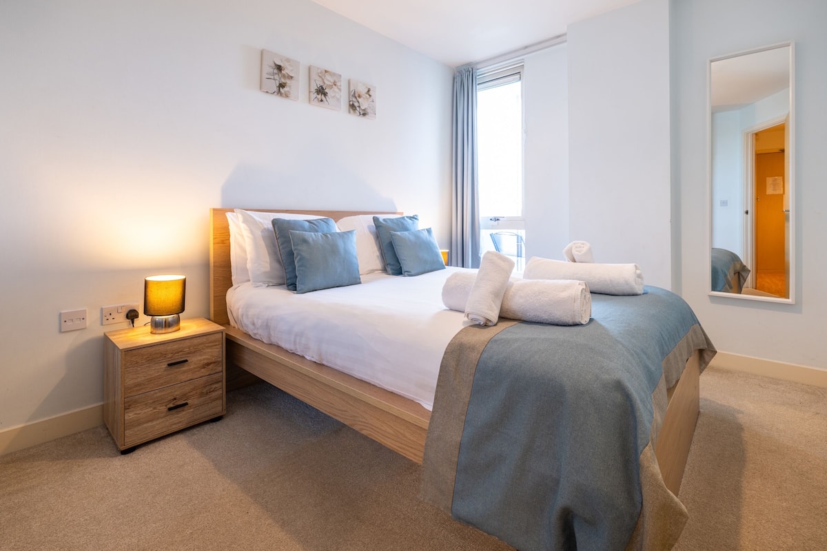 Un dormitorio ordenado con cama, mesita de noche y espejo.