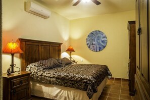 A bedroom with a bed, two bedside lamps, a wall clock, and a circular painting.