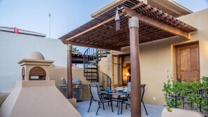 Un patio extérieur couvert, équipé d’une table et de chaises, d’un barbecue et d’un escalier en colimaçon.