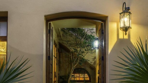 Un portail en arc mène à un patio abrité doté d’un sol en pierre, entouré de plantes en pot et agrémenté d’une lanterne fixée au mur.