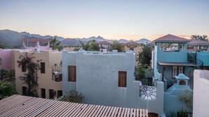 Un quartier résidentiel avec des maisons aux couleurs pastel, une terrasse en bois et une chaîne de montagnes en arrière-plan.
