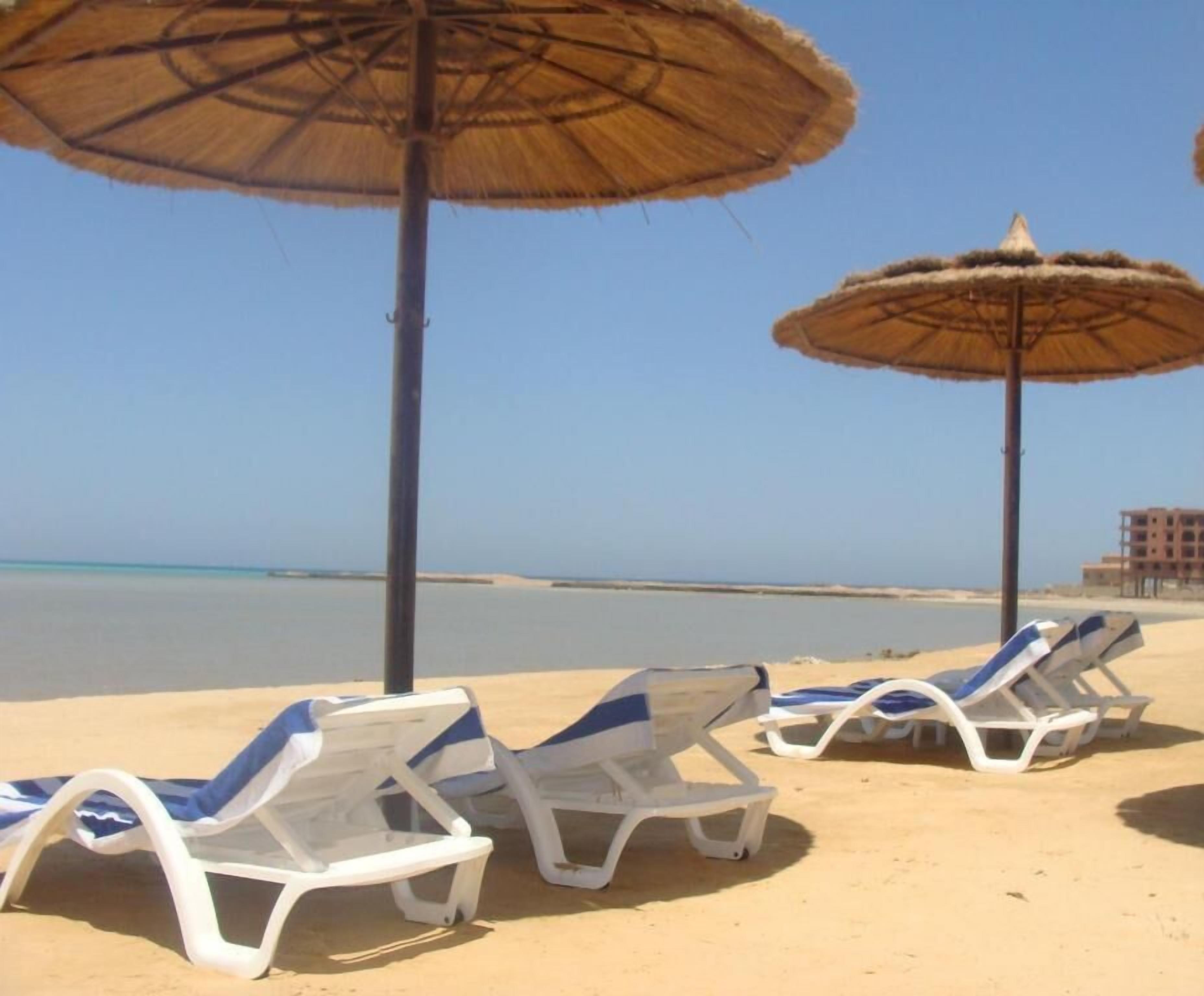 Une plage avec des chaises longues blanches et des parasols en chaume.