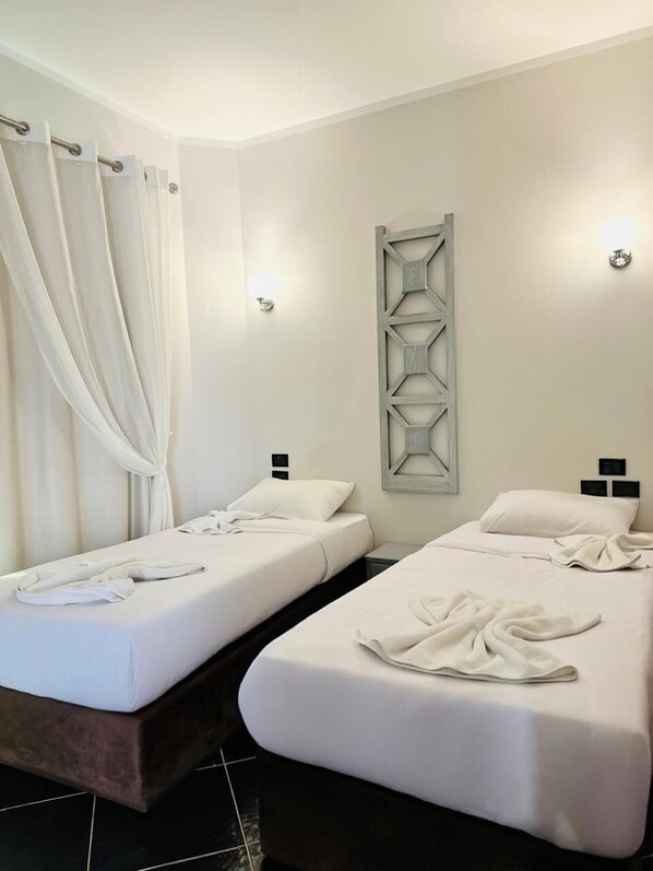 A hotel room with two single beds, a wooden headboard, a wall-mounted light fixture, and a curtain.
