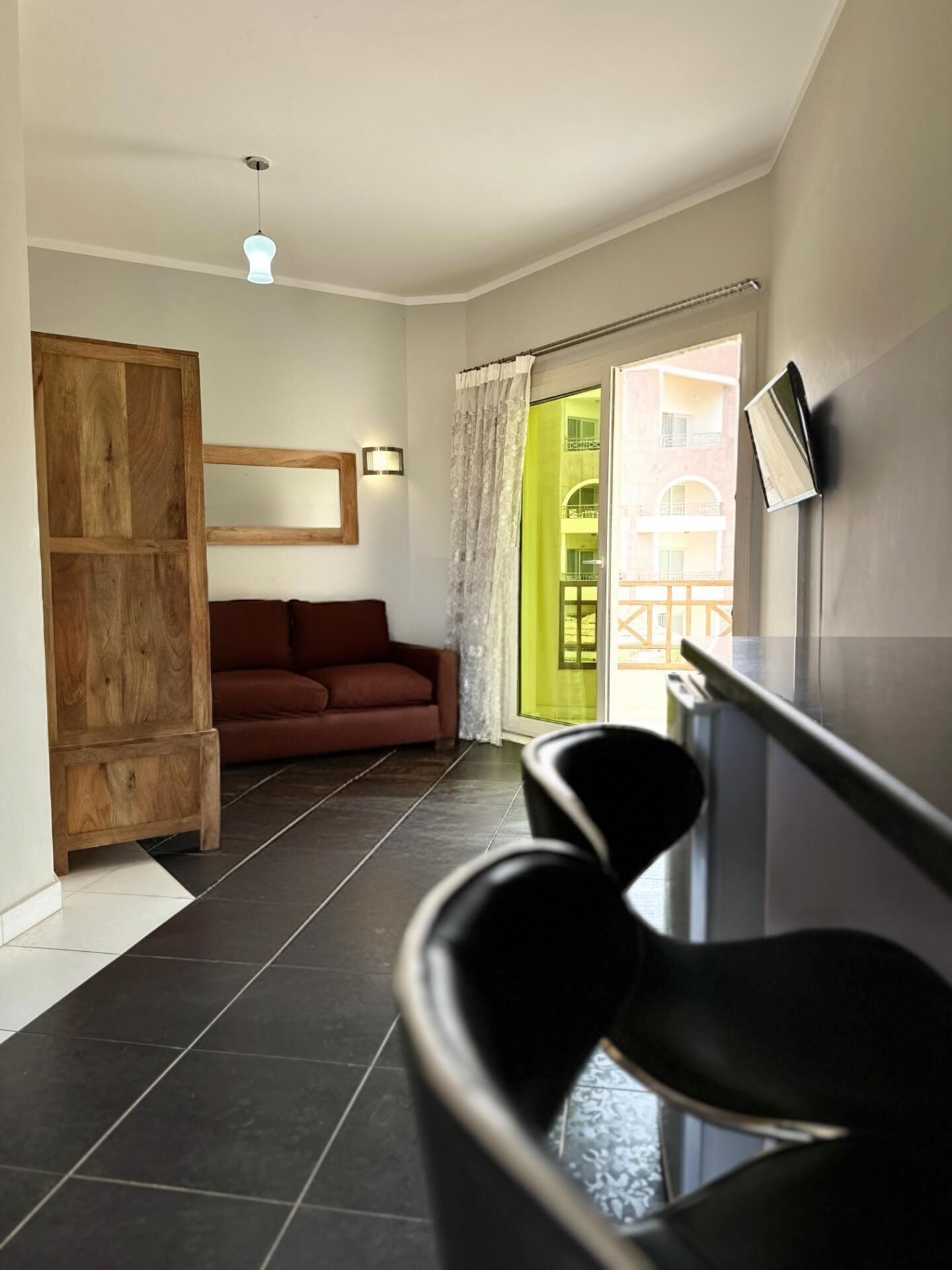 A modern interior with a dark tiled floor, a wooden cabinet, a brown sofa, and a black chair.