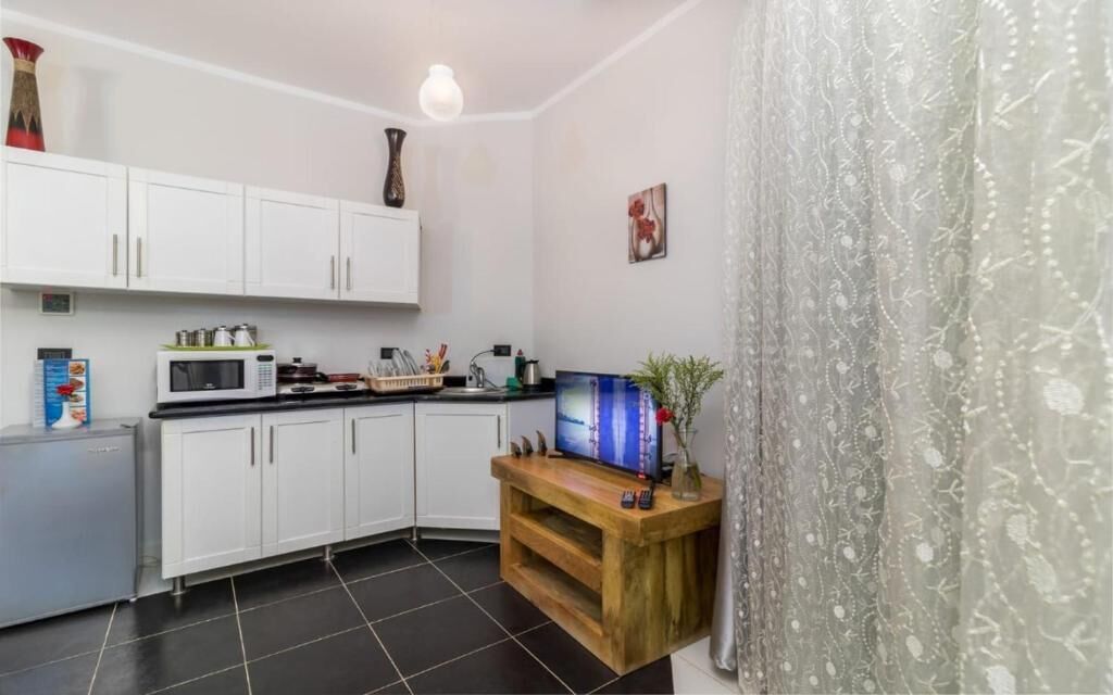 A compact kitchen with white cabinets, a microwave, a wooden counter, and a television.