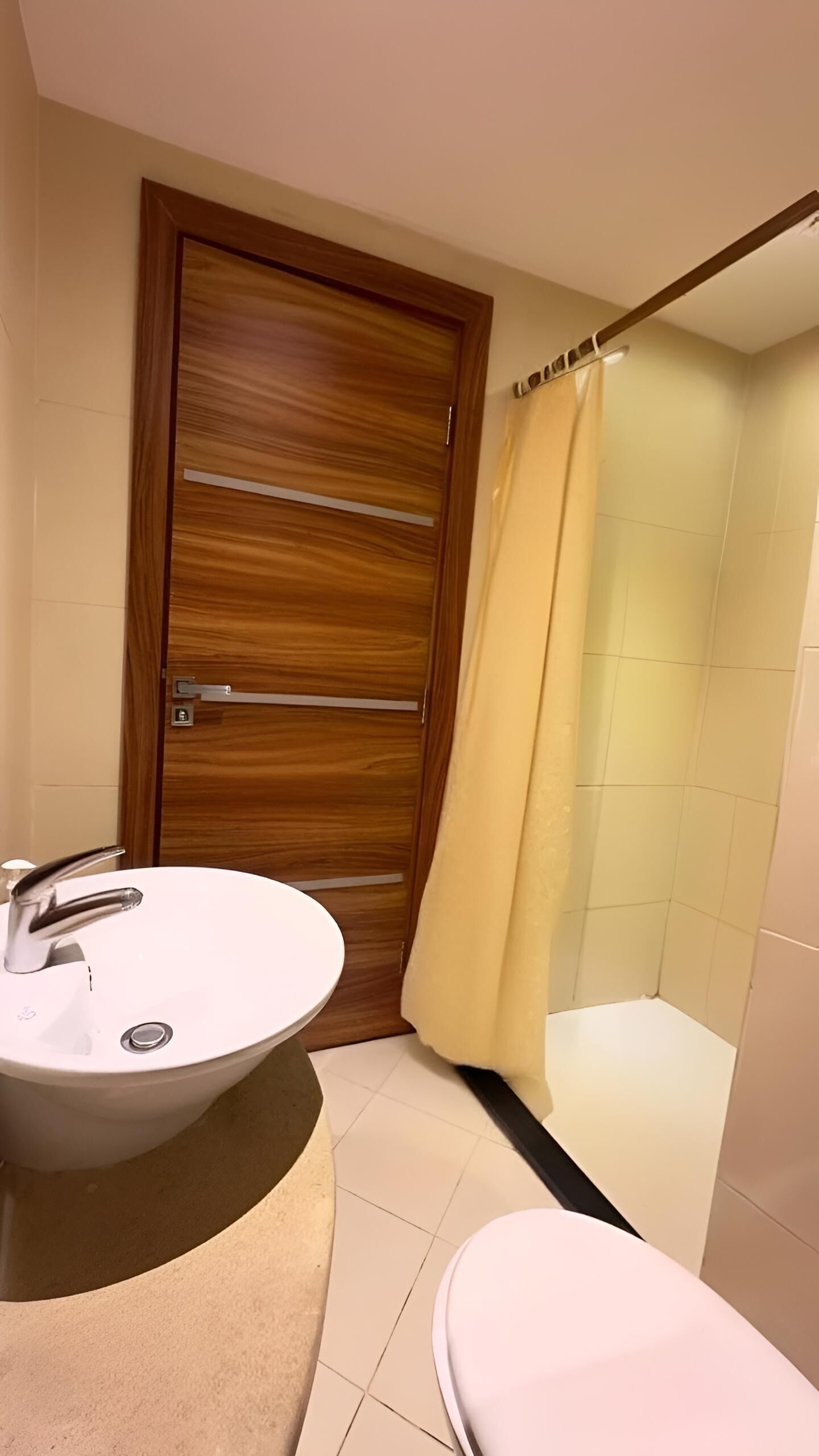 Un bany amb una porta de fusta, un lavabo blanc, un vàter i una zona de dutxa.