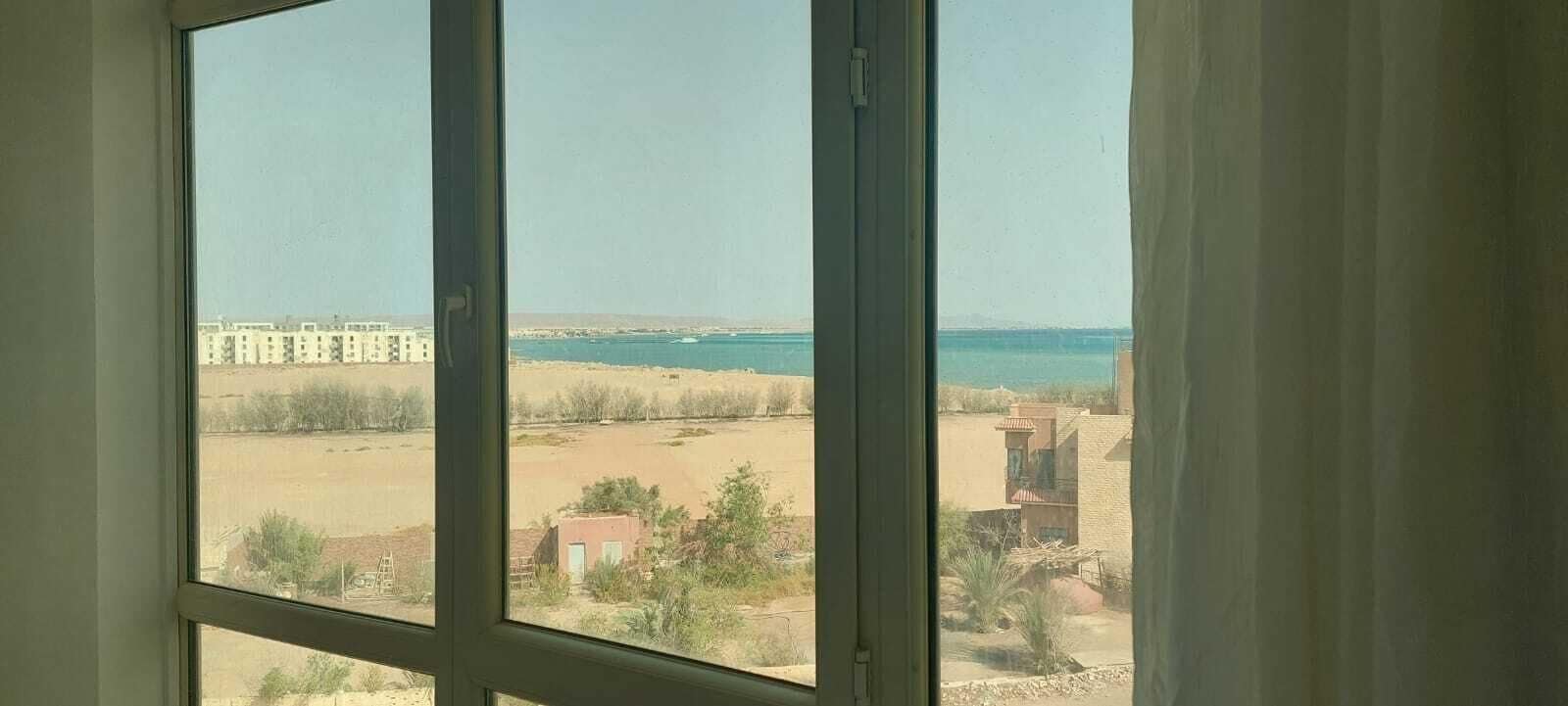 A room with a large window overlooking a beach and buildings.