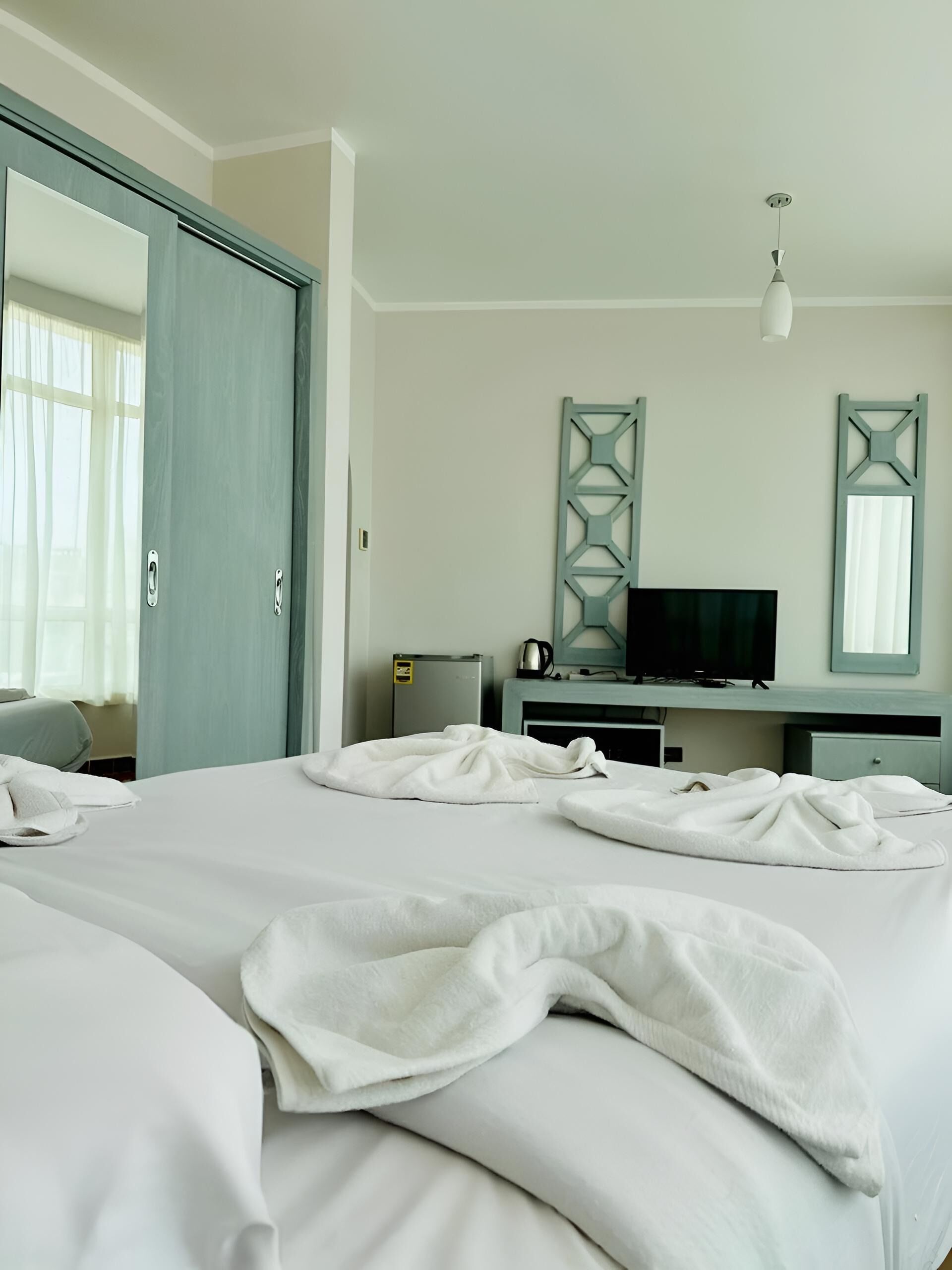 A hotel room with a large bed, a television, a desk, and a wardrobe.