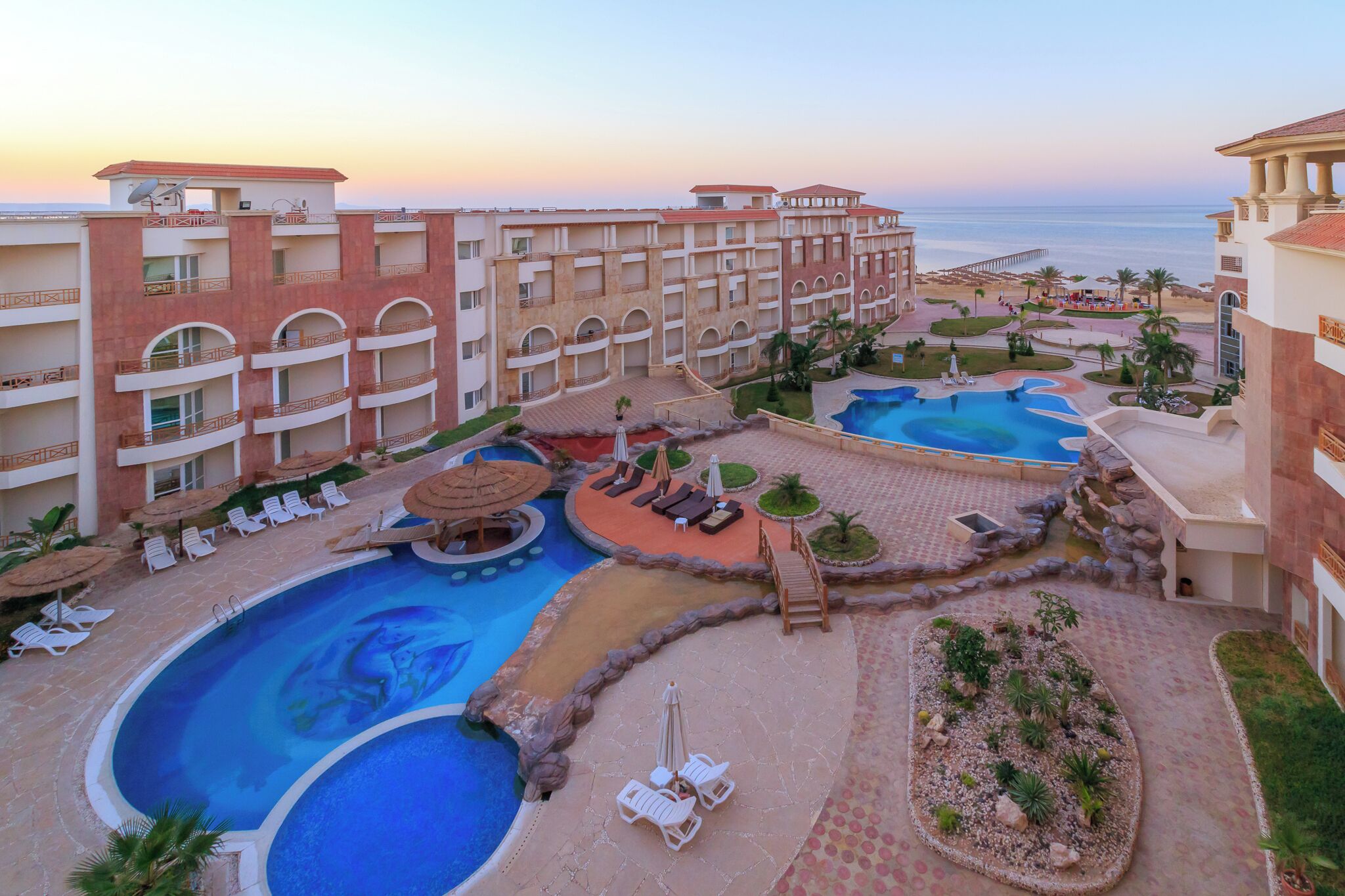 Een resort met meerdere zwembaden, ligbedden en een strandgedeelte.