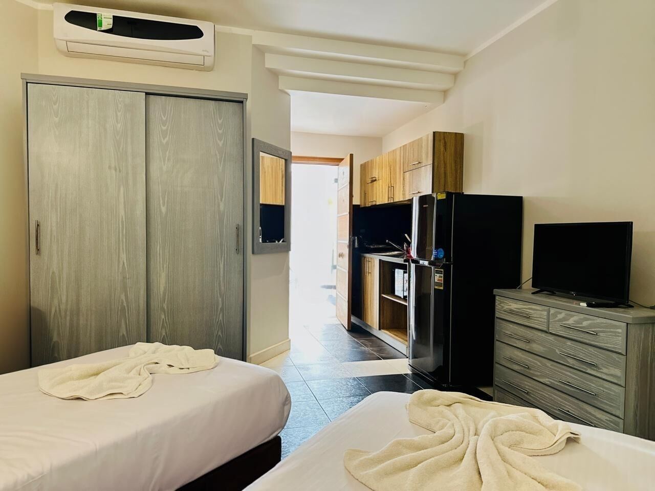 Une chambre d’hôtel avec deux lits, une armoire, un téléviseur et une kitchenette.