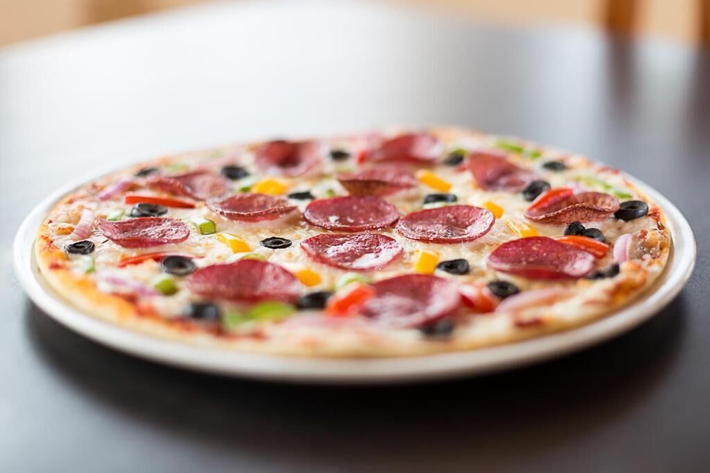A pizza with pepperoni, olives, and bell peppers on a white plate.