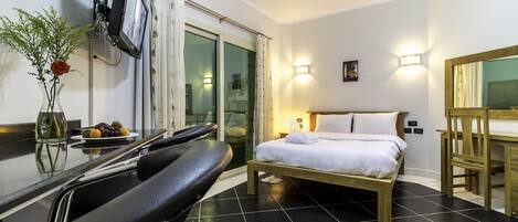 A hotel room with a bed, a desk, a chair, a small table with fruit, and a vase with a flower.
