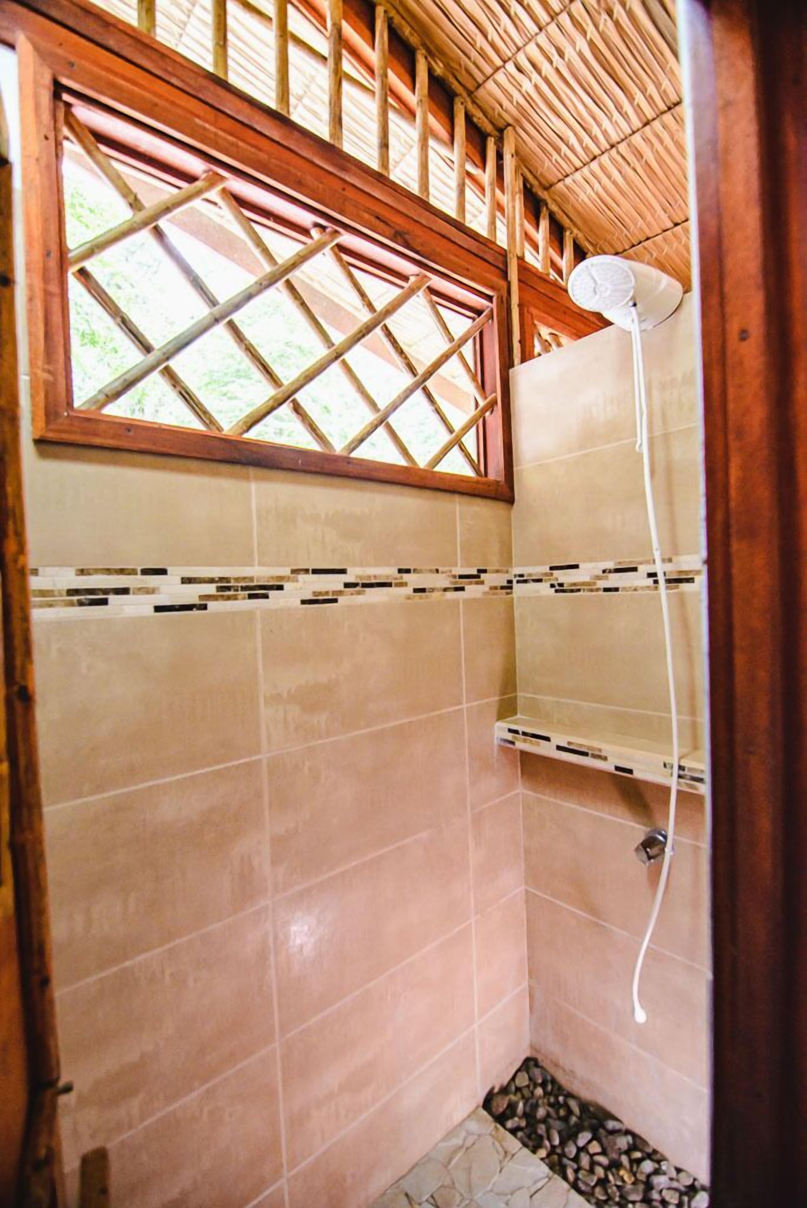 A small, tiled shower area with a wooden ceiling and a window with a lattice design.