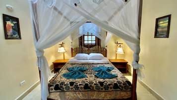 Una cama con dosel, dos lámparas de noche, una colcha estampada y una ventana con vistas.
