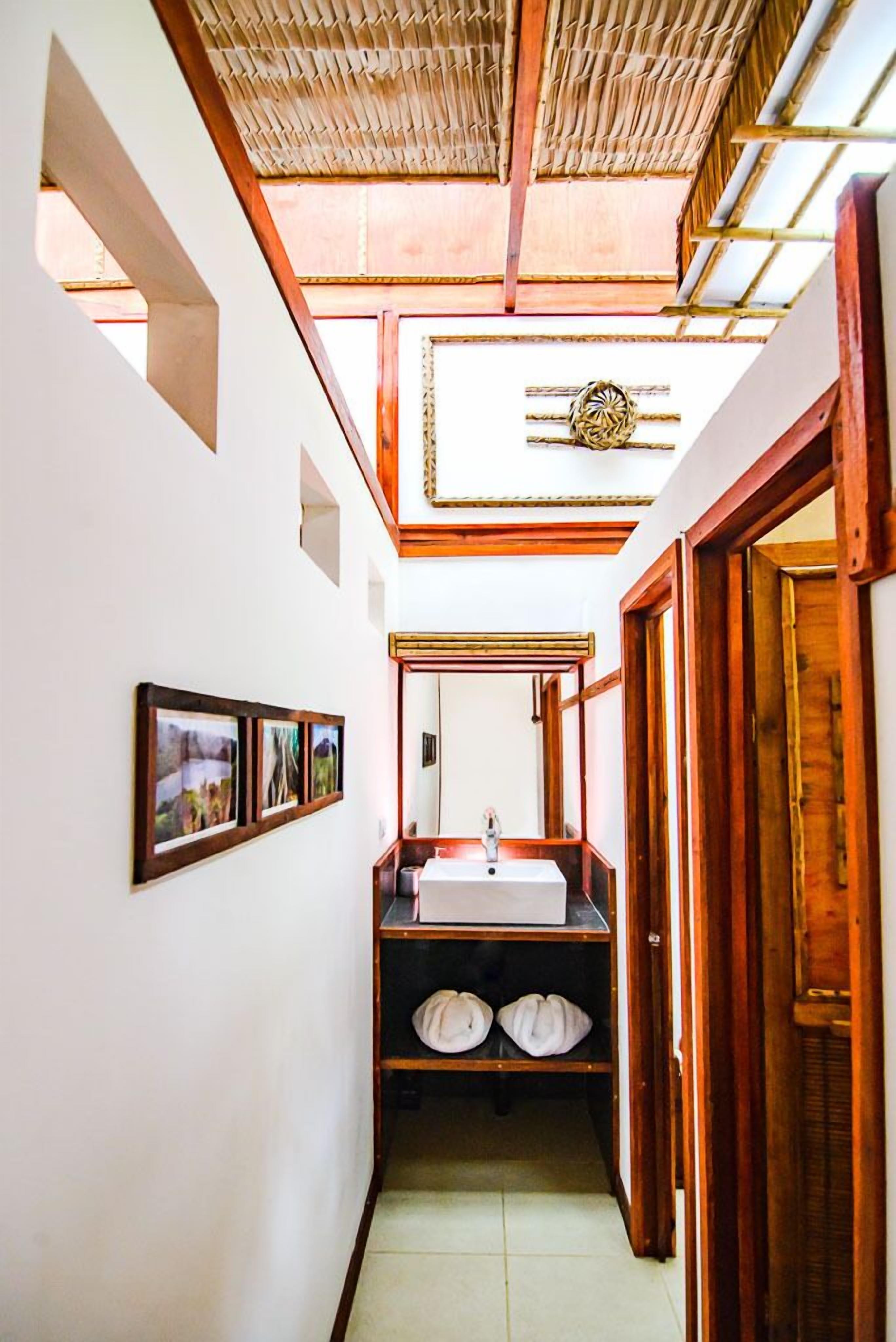 A narrow hallway with a wooden door on the right, a white sink with a mirror above it, and a woven ceiling.