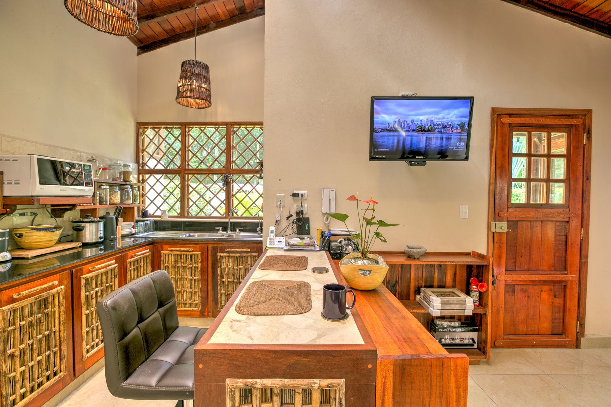 A kitchen with a wooden island, black leather chair, and a television on the wall.