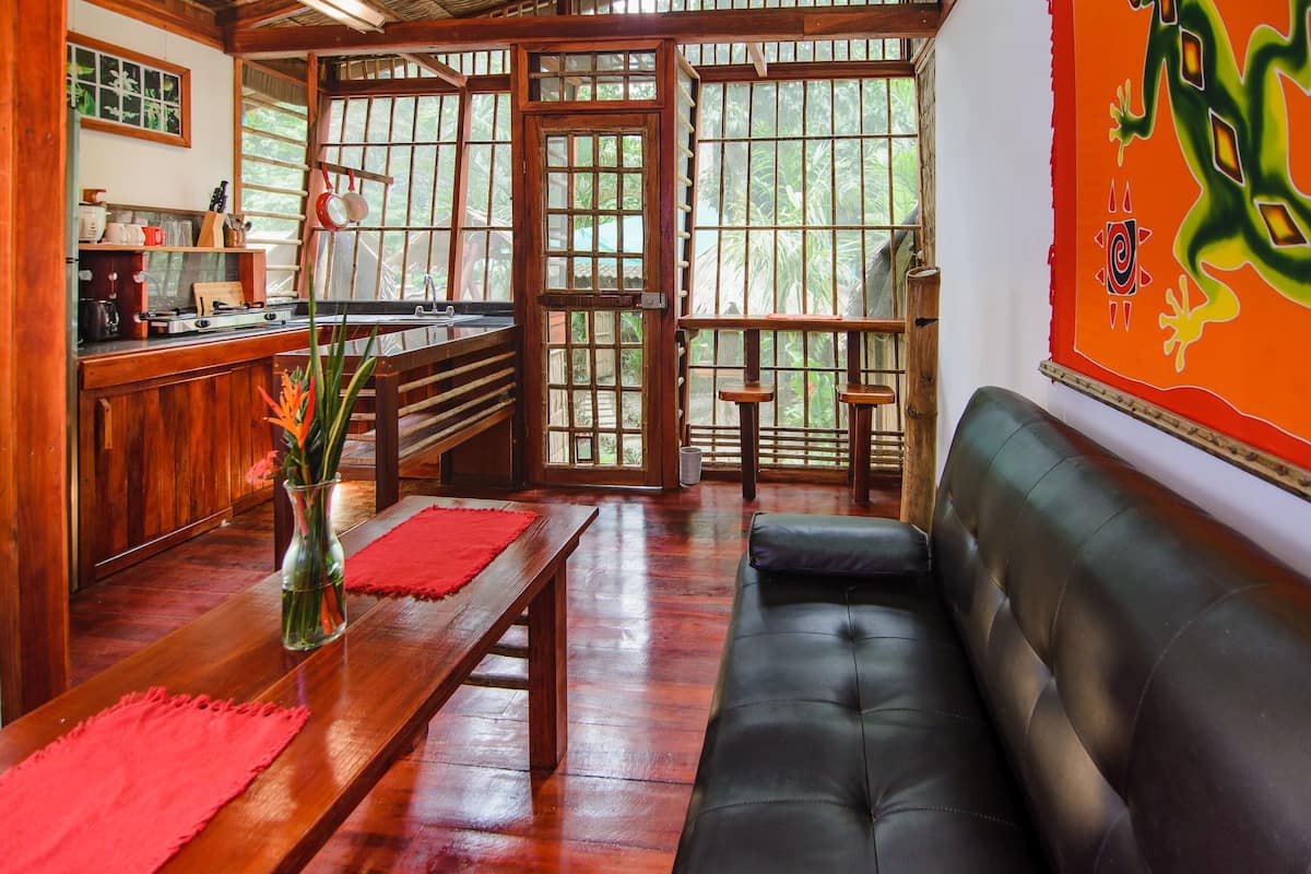 A cozy living area with a wooden bench, a black leather sofa, and a dining table with a red placemat.