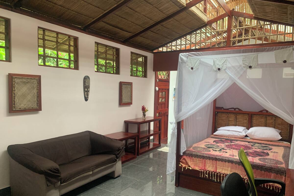A room with a bed under a canopy, a sofa, a small table, and decorative wall art.