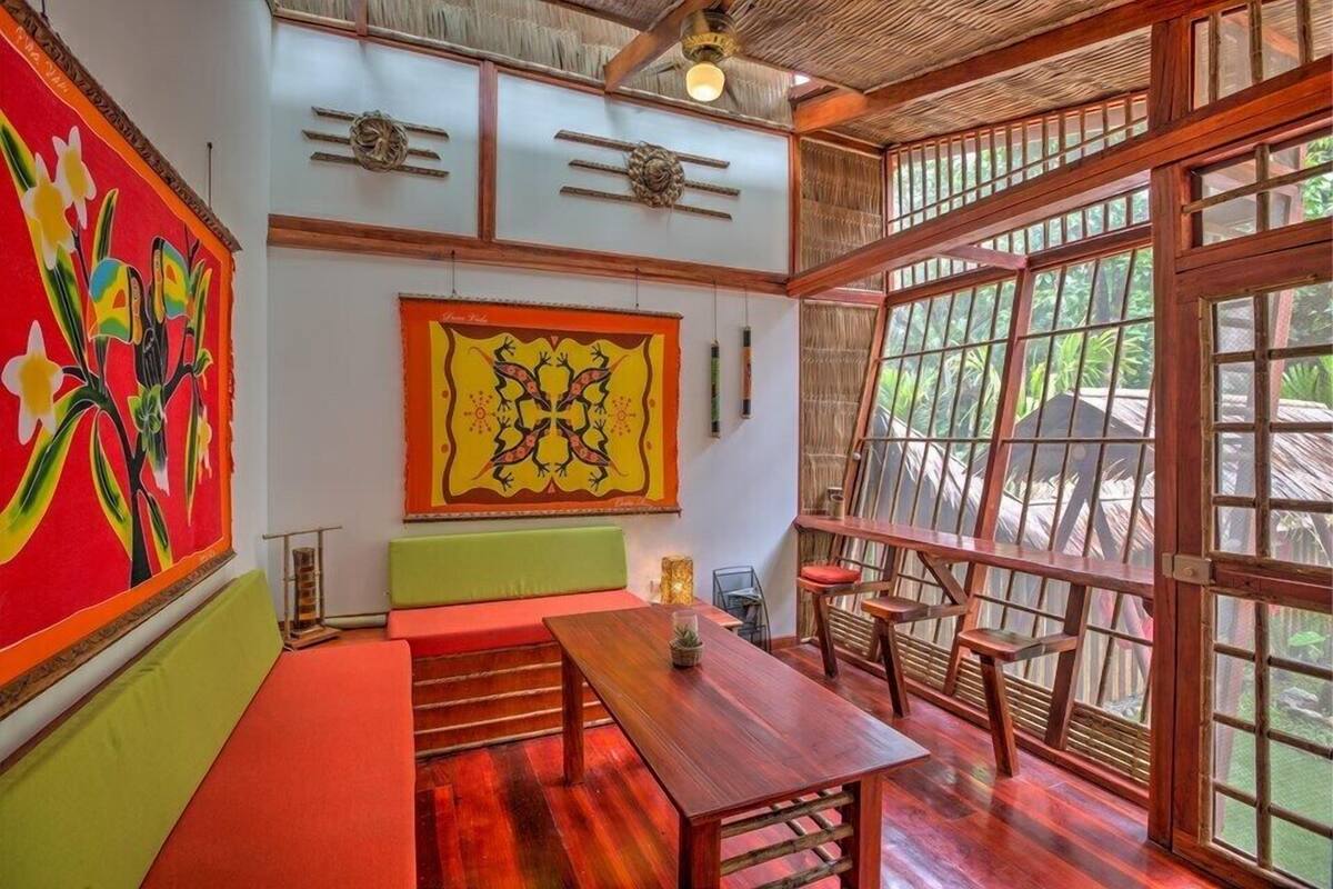 A room with a wooden table, benches, and a large window with a view of greenery.