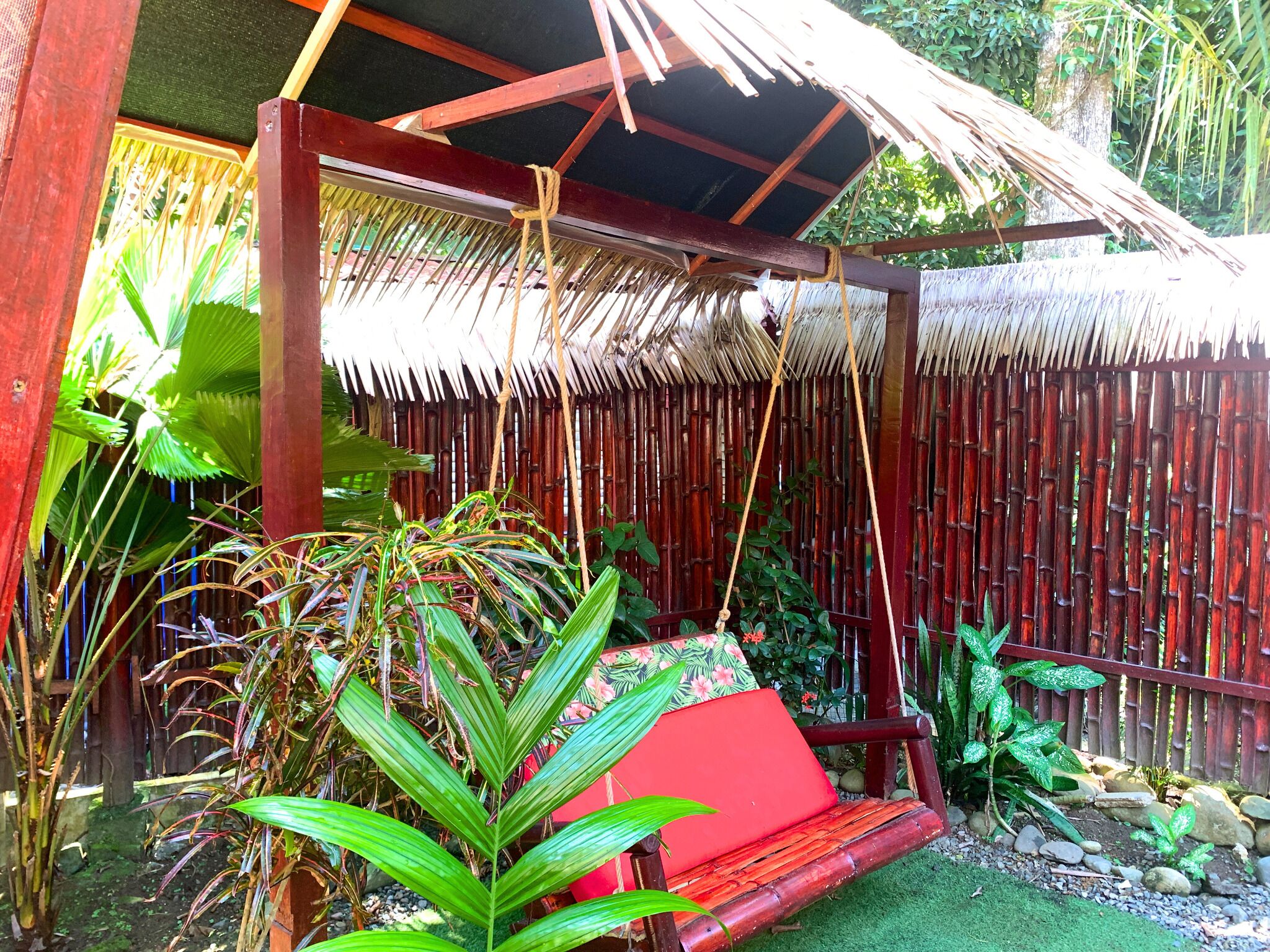 Un espacio de estar al aire libre techado, con un banco rojo y una estructura de techo de paja.
