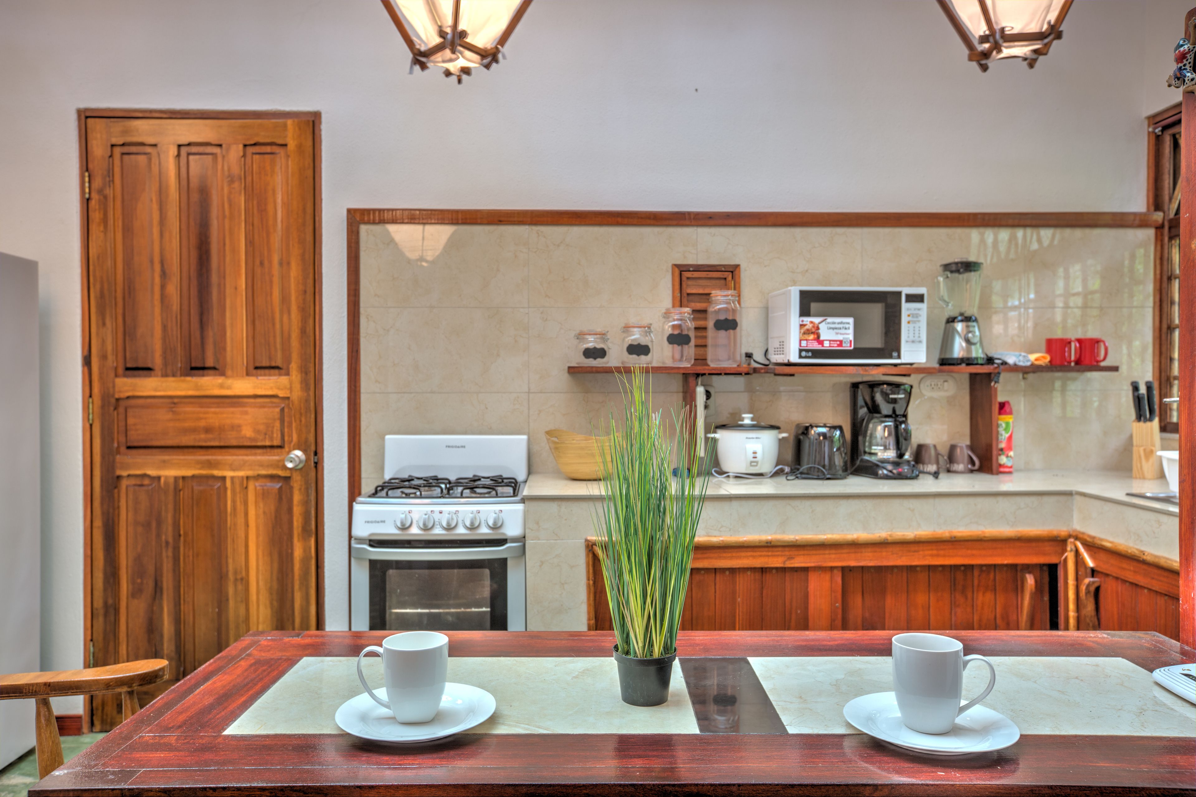 A kitchen with a wooden table, two white cups, and a potted plant.