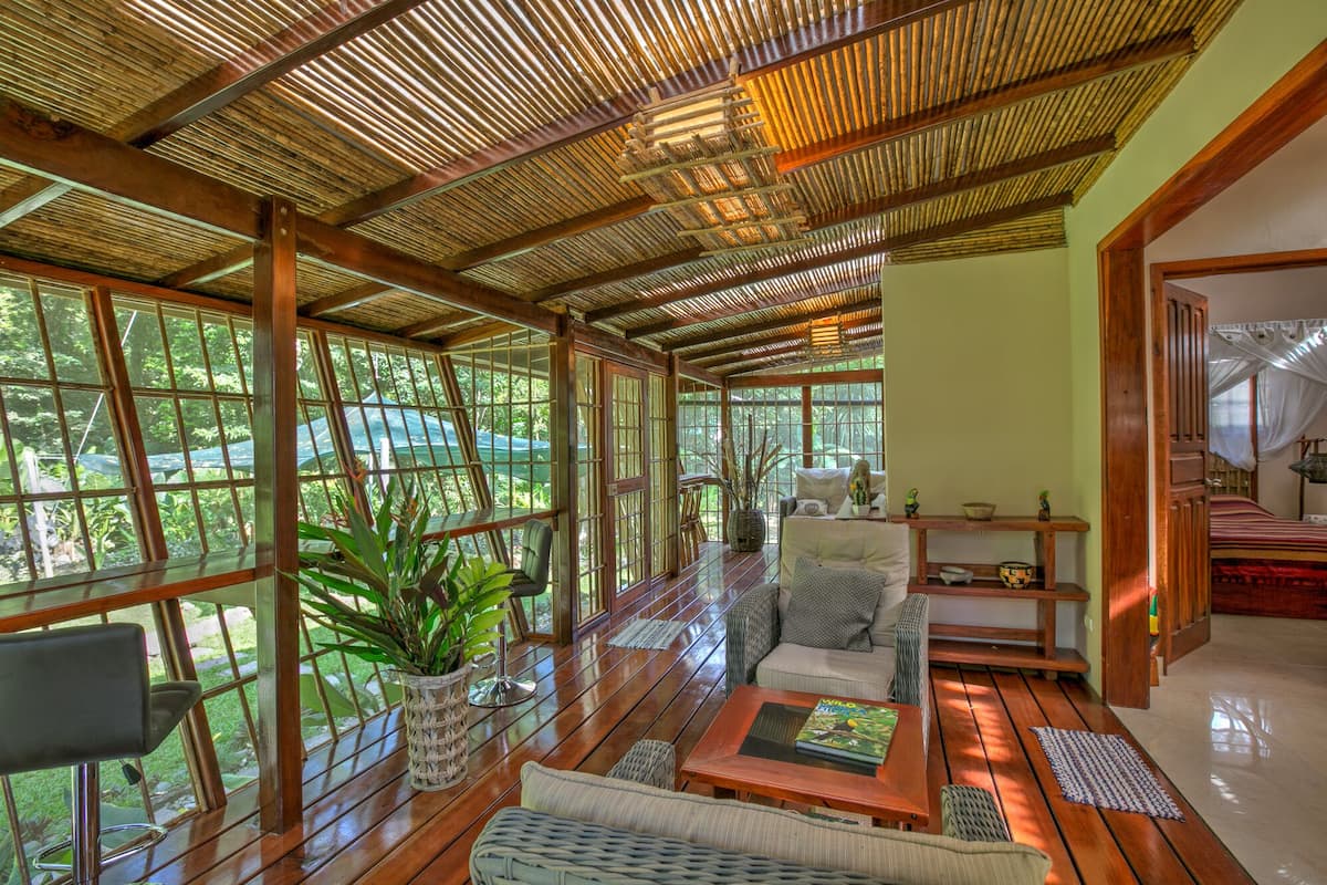 A spacious room with large windows, a wooden ceiling, and a cozy seating area with a sofa and chairs.