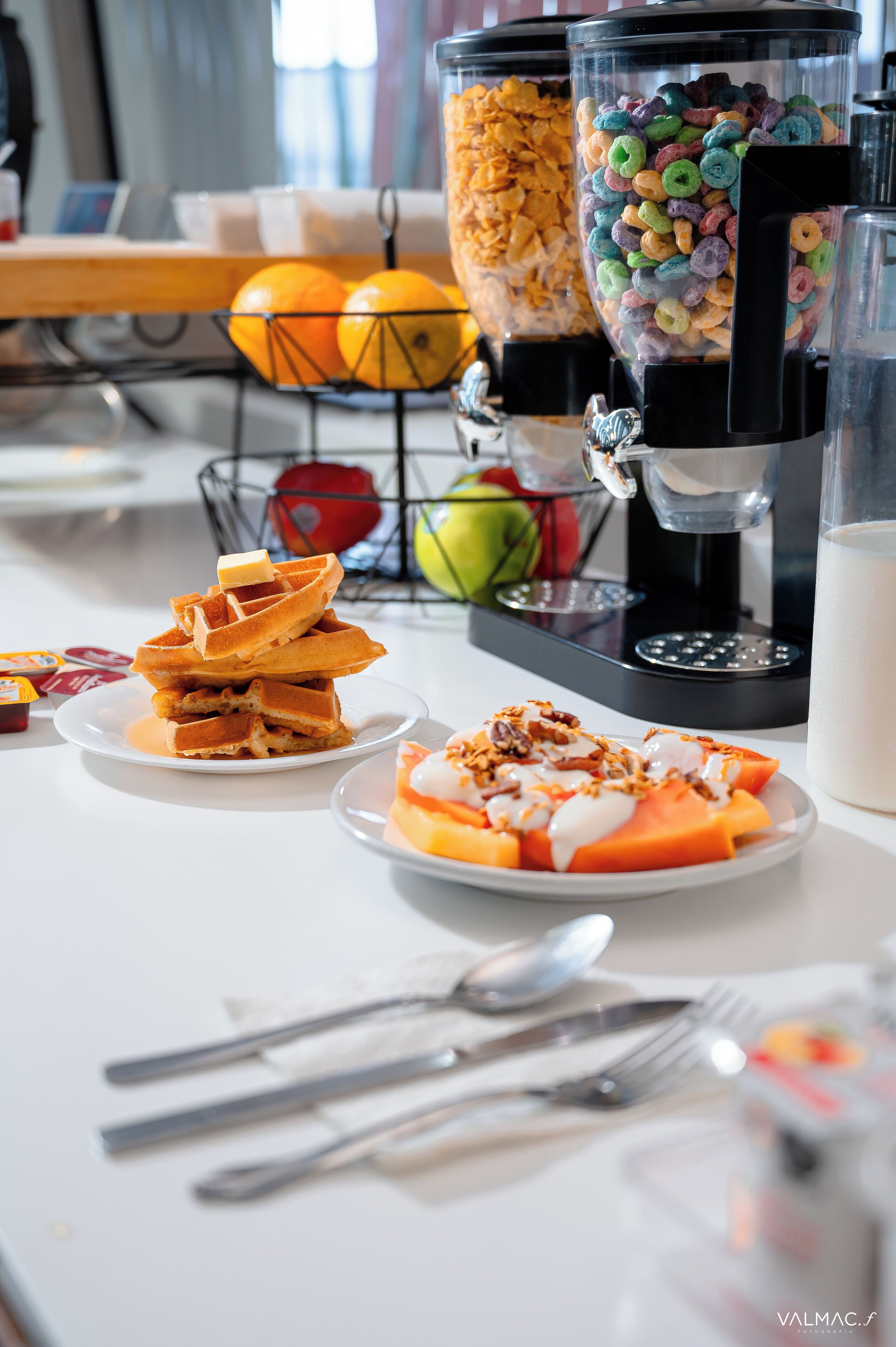 A breakfast buffet with waffles, cereal, and fruit.