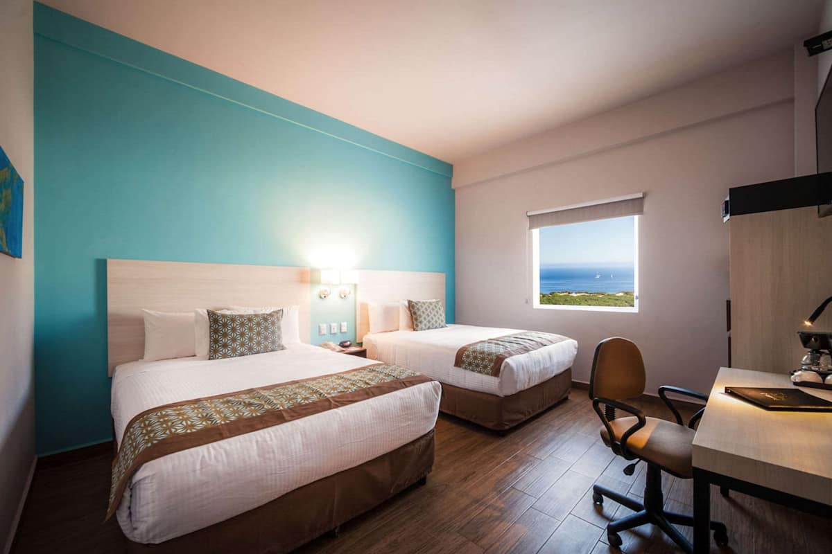 A hotel room with two beds, a desk, and a view of the sea.