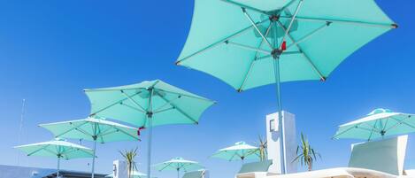 A row of white lounge chairs under turquoise umbrellas, arranged on a sunny beach.