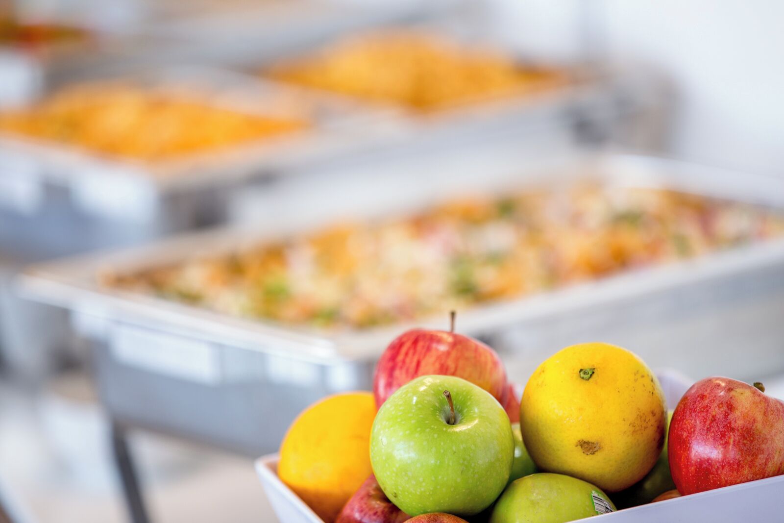 Un buffet proposant divers plats en arrière-plan et un saladier de fruits au premier plan.