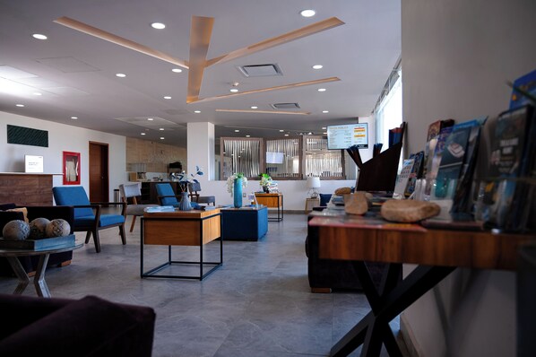 A modern hotel lobby with a reception desk, seating area, and a wall with informational posters.