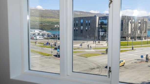 A modern building with a glass facade and a parking lot with cars and people. - Steinaskjól Apartments - Strandgata (Akureyri)