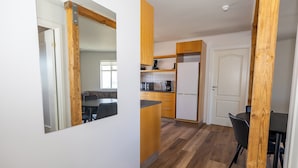 A modern kitchen with wooden cabinets, a refrigerator, and a dining area with chairs. - Steinaskjól Apartments - Strandgata (Akureyri)