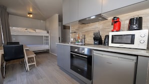 A compact kitchen with a microwave, coffee maker, and oven. There is a small dining table and a bunk bed in the adjacent room. - Steinaskjól Apartments - Strandgata (Akureyri)